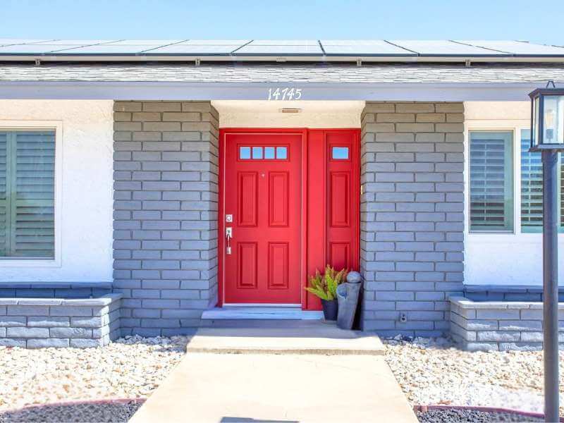 Single family home in Apple Valley CA featuring white exterior with gray trim, stone columns, and a bright red door.