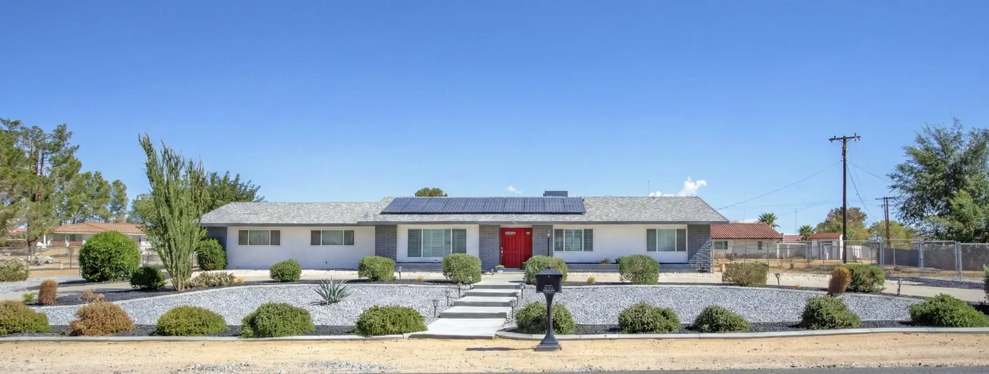 Apple Valley, CA Real Estate - Renovated single-family ranch home with solar panels, xeriscape landscaping, and a red front door.